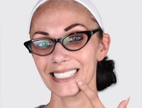 Smiling woman pointing at her white teeth after a successful dental aesthetics procedure and porcelain veneers placement.
